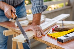 Adult craftsman carpenter with manual saw working on cutting a wooden table. Housework do it yourself. Stock photography.